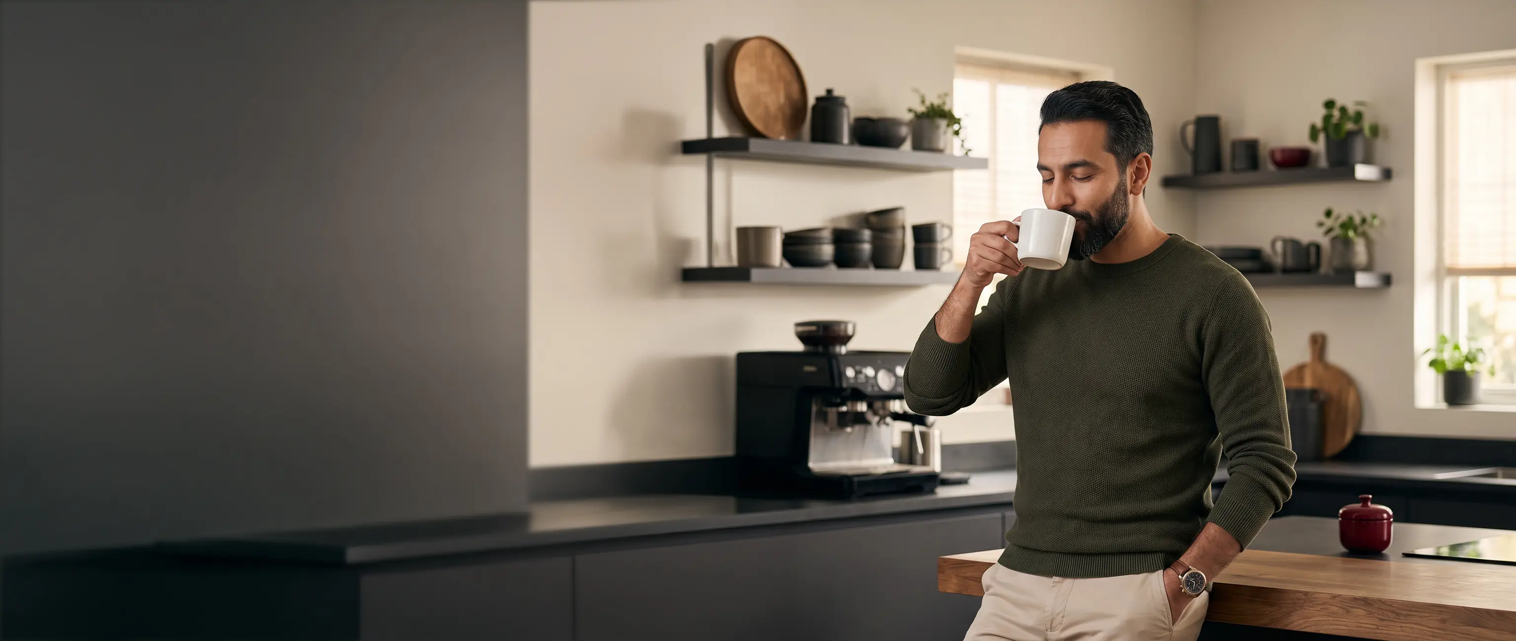 A relaxed man enjoying a cup of coffee in a luxurious modern kitchen, representing the financial peace of mind and secure lifestyle provided by National Bonds.