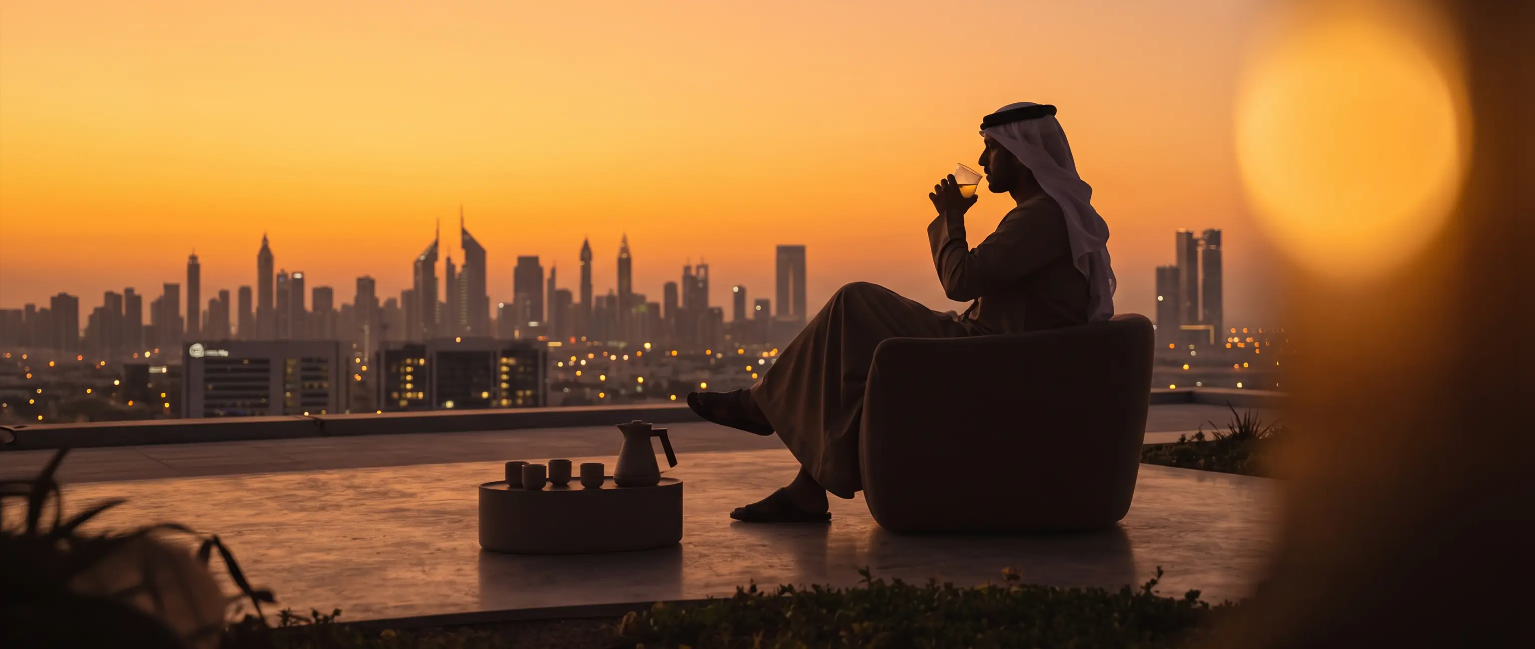 A man relaxing with coffee against the backdrop of the Dubai skyline at sunset, representing the financial peace of mind and secure future that comes with opening a new savings account with National Bonds.