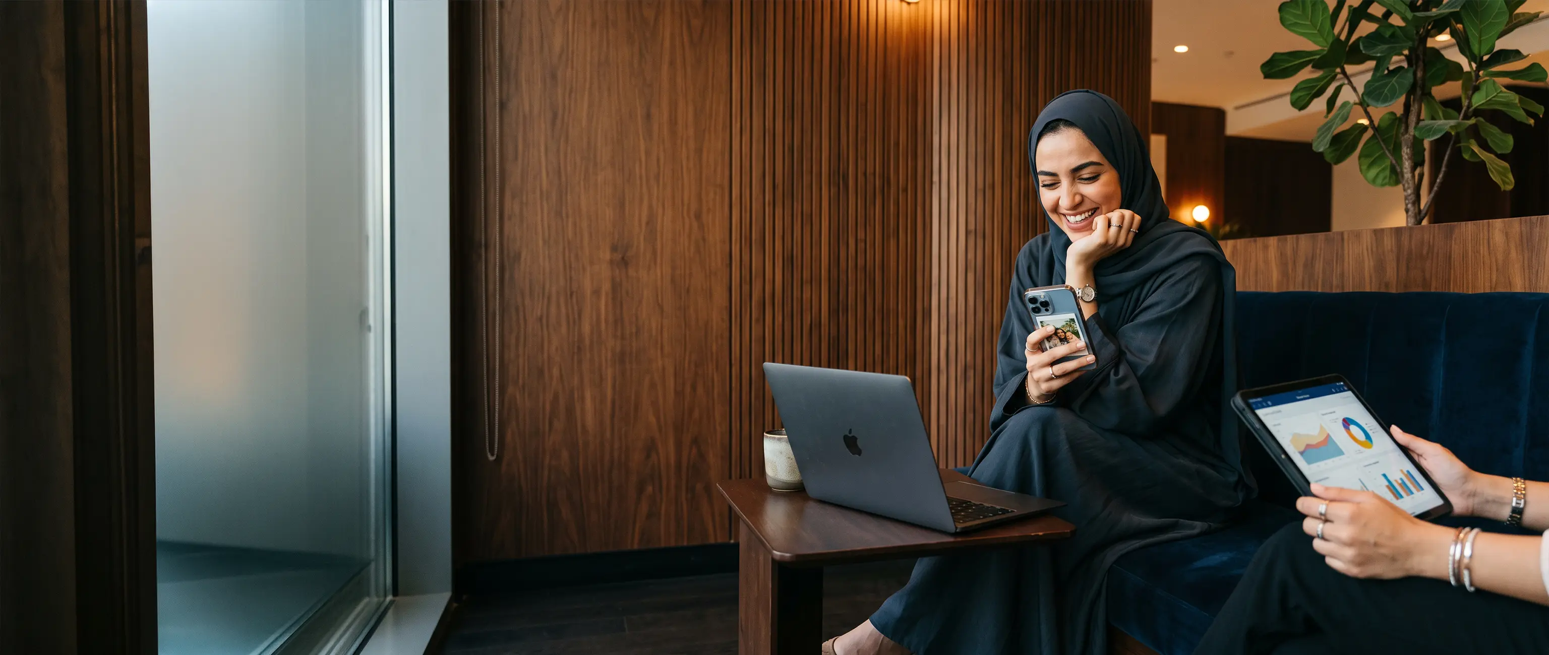 A smiling woman happily using her smartphone alongside digital financial charts, representing the ease and convenience of opening a new savings account online with National Bonds.