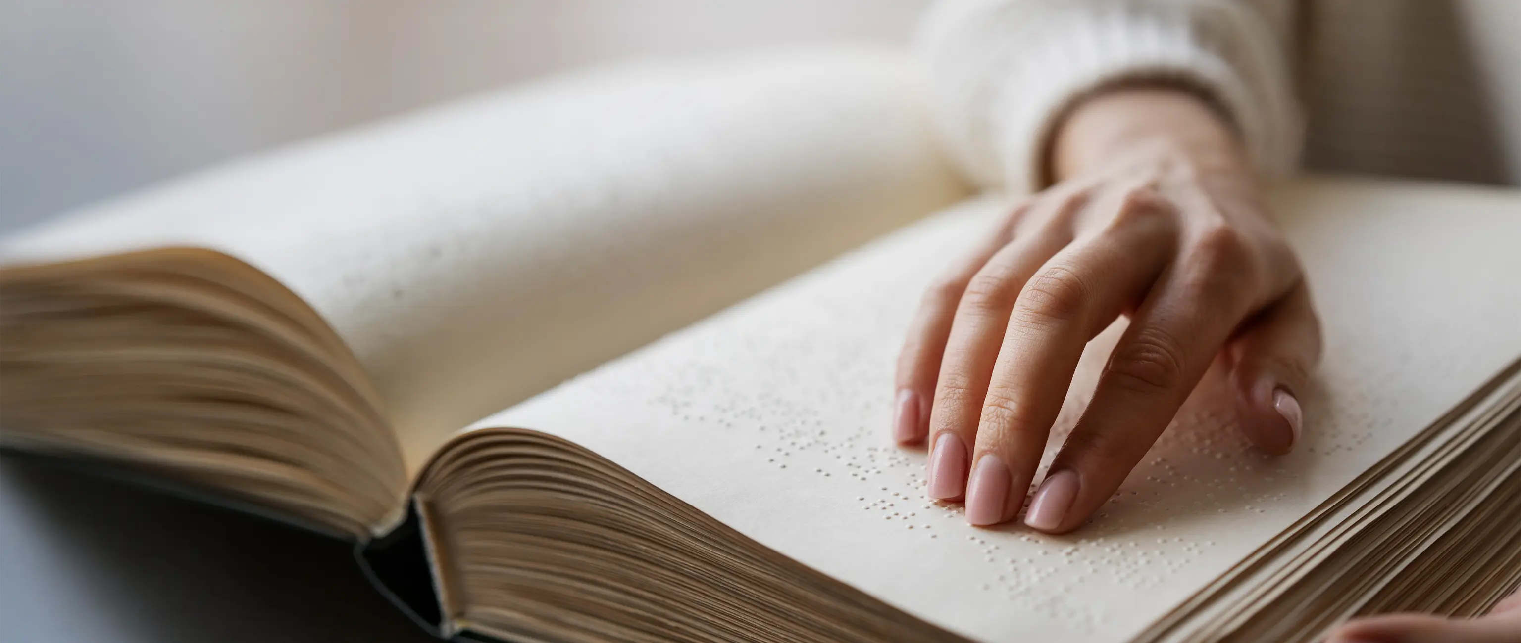 A hand reading a Braille book, representing charitable initiatives to support the blind and visually impaired with Waqf Al Noor from National Bonds.