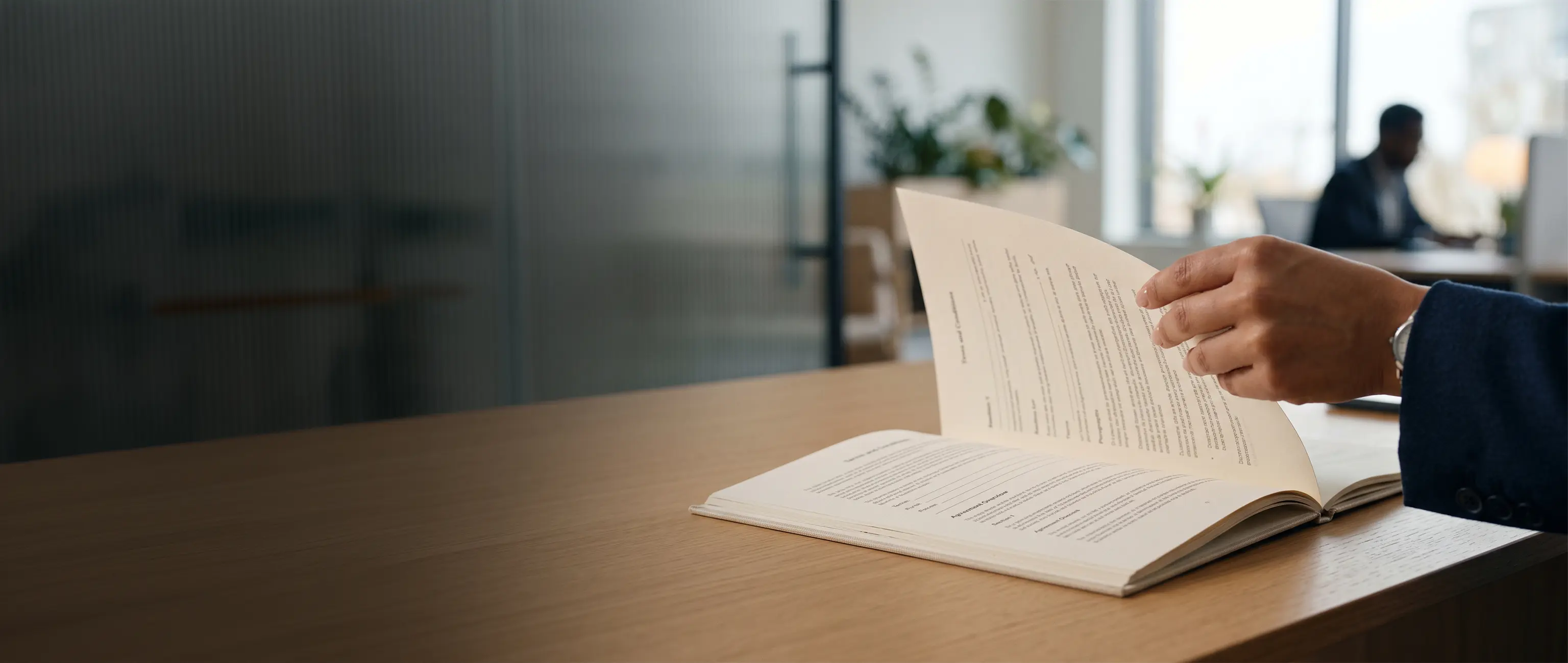 A professional turning the pages of the National Bonds Terms of Use document on a wooden office desk.